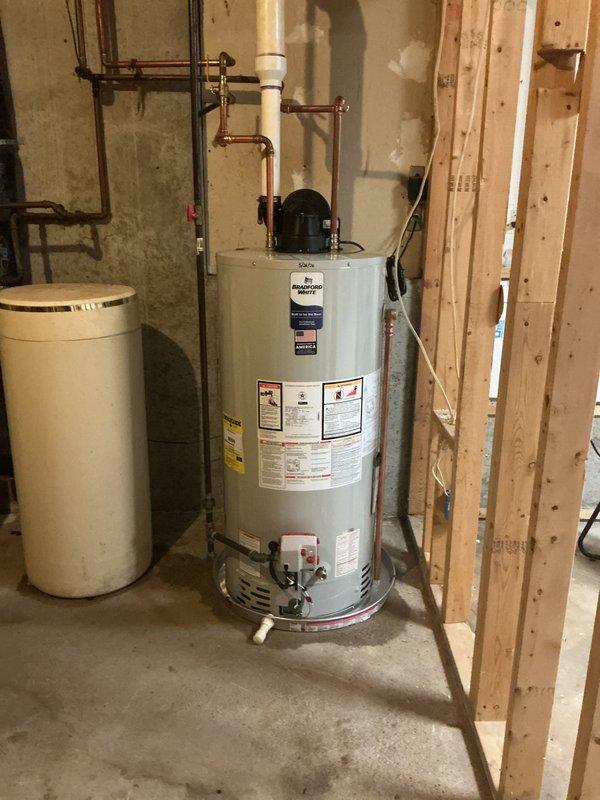 Completed installation of 50-gallon power vent water heater in basement utility area. Installed new copper supply piping with shut-off valves, configured proper venting system using white PVC pipe with 90-degree elbow transition from vertical to horizontal run, and mounted power vent motor assembly on top of unit. All connections tested and verified operational, with customer payment processed via credit card.