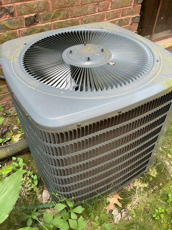 Completed comprehensive AC tune-up on 19-year-old residential air conditioning system in preparation for cooling season. Performed standard maintenance procedures including inspection of condenser unit, cleaning of coils, verification of refrigerant levels, testing of electrical components, and assessment of overall system operation. System found to be functioning properly with all components operating within normal parameters. Discussed equipment age considerations and future replacement planning with homeowner given the unit's advanced service life. Documentation photos captured showing outdoor condenser unit positioned against brick wall with visible weathering consistent with age, horizontal louvered fins, and circular top-mounted fan grille in good structural condition.