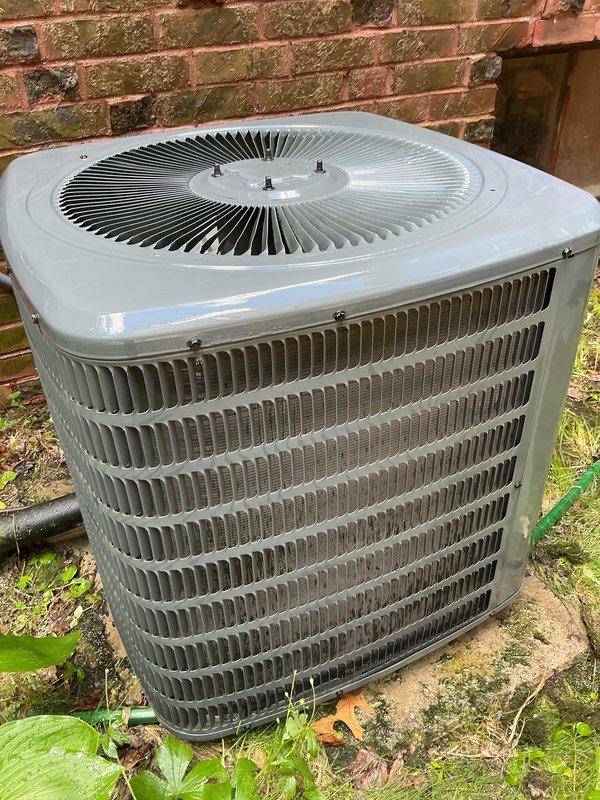 Completed comprehensive AC tune-up on 19-year-old residential air conditioning system in preparation for cooling season. Performed standard maintenance procedures including inspection of condenser unit, cleaning of coils, verification of refrigerant levels, testing of electrical components, and assessment of overall system operation. System found to be functioning properly with all components operating within normal parameters. Discussed equipment age considerations and future replacement planning with homeowner given the unit's advanced service life. Documentation photos captured showing outdoor condenser unit positioned against brick wall with visible weathering consistent with age, horizontal louvered fins, and circular top-mounted fan grille in good structural condition.