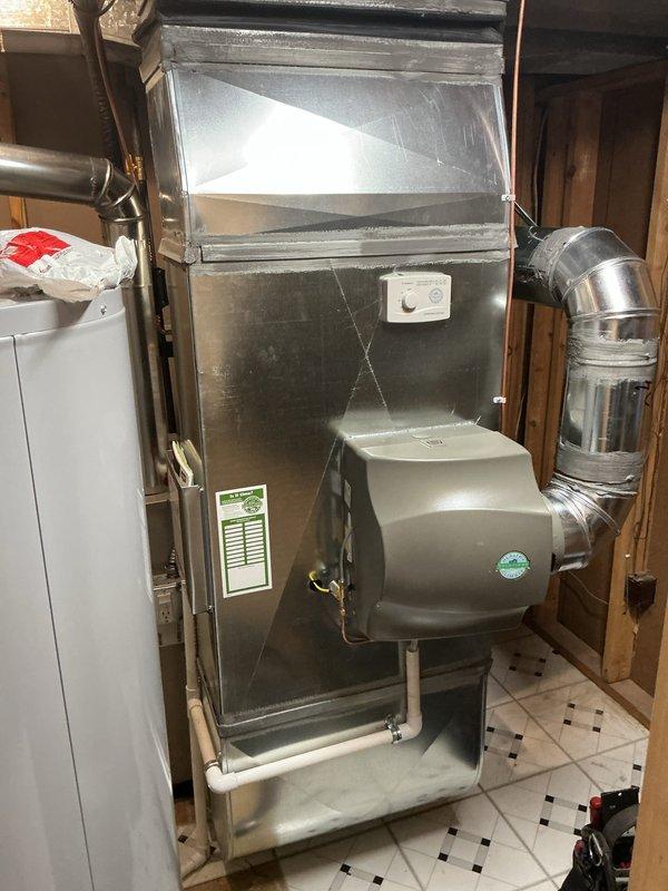 Completed full HVAC system installation in residential basement utility area, including new furnace unit with integrated humidifier system and complete ductwork configuration. Installed metal supply and return ductwork with proper sealing and connections, routed flexible ductwork and conduit lines, and mounted humidifier unit with PVC drainage piping. System placed on drain pan with all components properly connected, labeled, and tested for operational readiness.