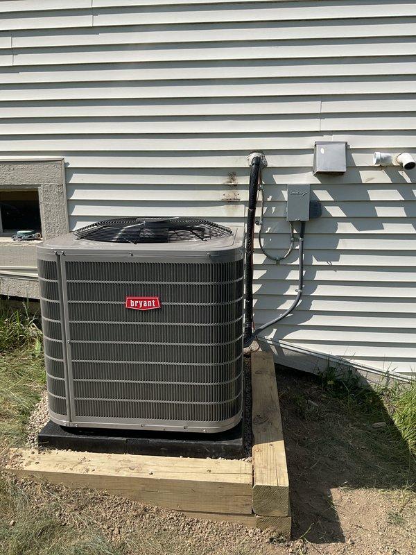Completed full HVAC system installation including new Bryant condensing unit and furnace with associated venting and refrigerant lines. Unit mounted on wooden platform with proper electrical disconnect, PVC vent piping installed through exterior wall, and all connections tested for proper operation.