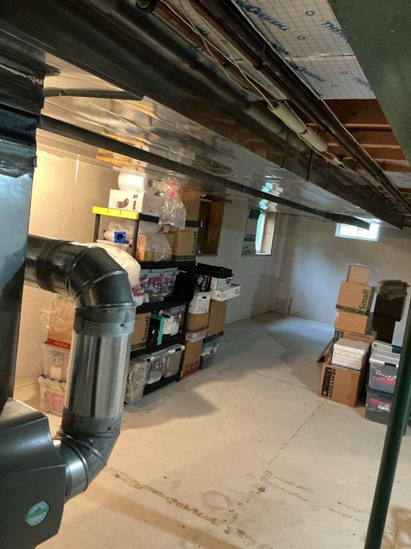 Responded to no cooling complaint at residential property. Upon arrival, inspected HVAC system located in basement utility area. Evaluated air conditioning unit and associated ductwork system. Documented existing conditions including water heater proximity to HVAC components and basement storage configuration affecting system accessibility. Verified ductwork connections and assessed airflow pathways through black PVC and metal duct components. Coordinated with property representative regarding necessary repairs to restore proper cooling function.