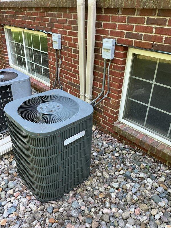Responded to service call for air conditioning system not cooling properly with water puddle observed near equipment. Upon arrival, inspected two exterior condensing units positioned on river rock bed against brick residential structure. Noted signs of moisture accumulation among rocks surrounding units and evidence of algae/moss growth indicating ongoing water discharge issue. Performed diagnostic assessment of refrigerant lines, electrical connections, and condensate drainage system to identify source of cooling deficiency and water leakage.