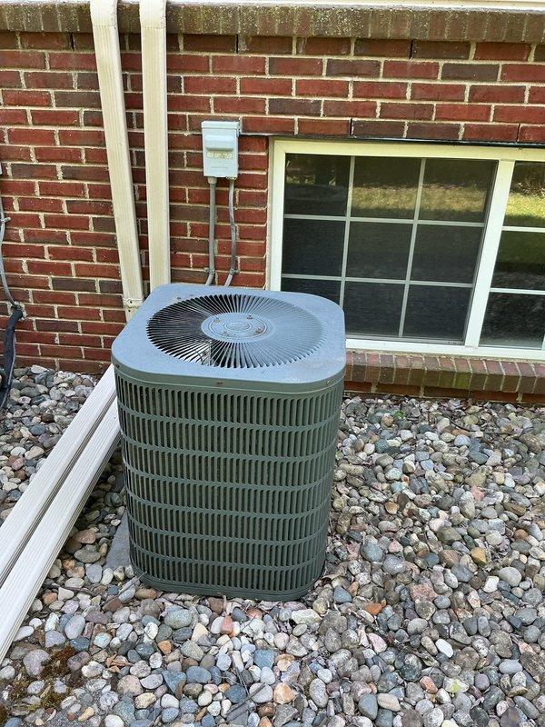 Responded to service call for air conditioning system not cooling properly with water puddle observed near equipment. Upon arrival, inspected two exterior condensing units positioned on river rock bed against brick residential structure. Noted signs of moisture accumulation among rocks surrounding units and evidence of algae/moss growth indicating ongoing water discharge issue. Performed diagnostic assessment of refrigerant lines, electrical connections, and condensate drainage system to identify source of cooling deficiency and water leakage.