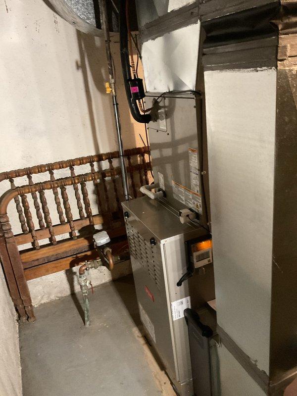 Successfully installed two furnace units and one air conditioning system in basement utility area. First furnace unit mounted on wall with proper electrical connections via black conduit, while second furnace positioned on concrete floor. Both units secured according to manufacturer specifications with all required labels visible and accessible. Connected ductwork to ceiling-mounted distribution system utilizing existing infrastructure. Verified proper clearances from surrounding walls and stored items for safe operation and future maintenance access. Completed all electrical connections, tested system startup sequences, and confirmed operational status of both heating units and cooling system.