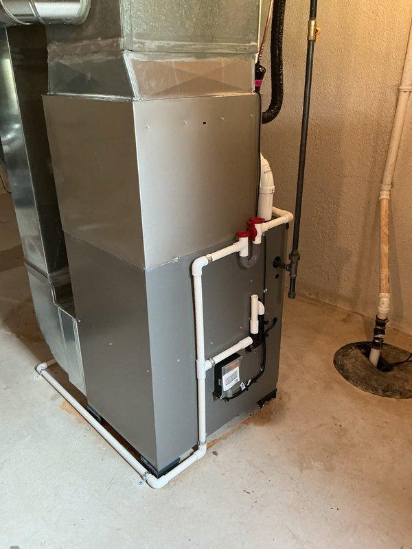 Completed installation of new air conditioning system with evaporator coil in residential utility room. Installed furnace unit with integrated air handler, connected white PVC condensate drainage lines with shutoff valve, and routed refrigerant lines to outdoor condenser unit. Verified proper airflow through ductwork connections, tested system operation, and confirmed all components functioning within manufacturer specifications.
