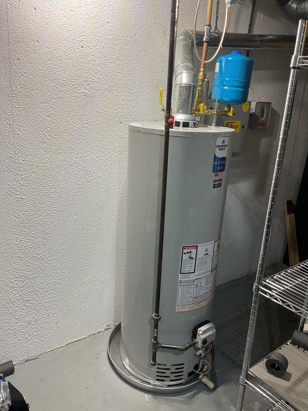 Completed installation of 50-gallon gas water heater in residential basement utility area. Installed new unit with proper venting, connected copper water supply lines with yellow-handled shut-off valves, and mounted blue expansion tank horizontally at top of unit. Installed temperature and pressure relief valve with orange discharge pipe running vertically alongside tank, verified all connections for leaks, and ensured proper clearances for maintenance access and code compliance.