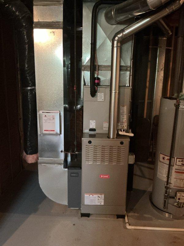 Completed full HVAC system installation including Bryant furnace, air conditioning unit with evaporator coil, and humidifier in residential basement mechanical room. All equipment properly positioned, connected to existing ductwork, and integrated with plumbing systems. Copper refrigerant lines installed and routed from outdoor condensing unit to indoor evaporator coil. Furnace cabinet secured with all manufacturer labels and safety documentation intact. Humidifier integrated into supply duct system with water supply connection established. PVC condensate drain lines installed and routed appropriately. All electrical connections completed per manufacturer specifications and local code requirements. System tested for proper operation including airflow, refrigerant pressures, and heating cycles. Equipment startup procedures performed and all systems verified operational.