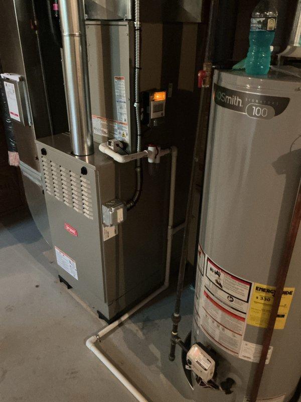 Completed full HVAC system installation including Bryant furnace, air conditioning unit with evaporator coil, and humidifier in residential basement mechanical room. All equipment properly positioned, connected to existing ductwork, and integrated with plumbing systems. Copper refrigerant lines installed and routed from outdoor condensing unit to indoor evaporator coil. Furnace cabinet secured with all manufacturer labels and safety documentation intact. Humidifier integrated into supply duct system with water supply connection established. PVC condensate drain lines installed and routed appropriately. All electrical connections completed per manufacturer specifications and local code requirements. System tested for proper operation including airflow, refrigerant pressures, and heating cycles. Equipment startup procedures performed and all systems verified operational.