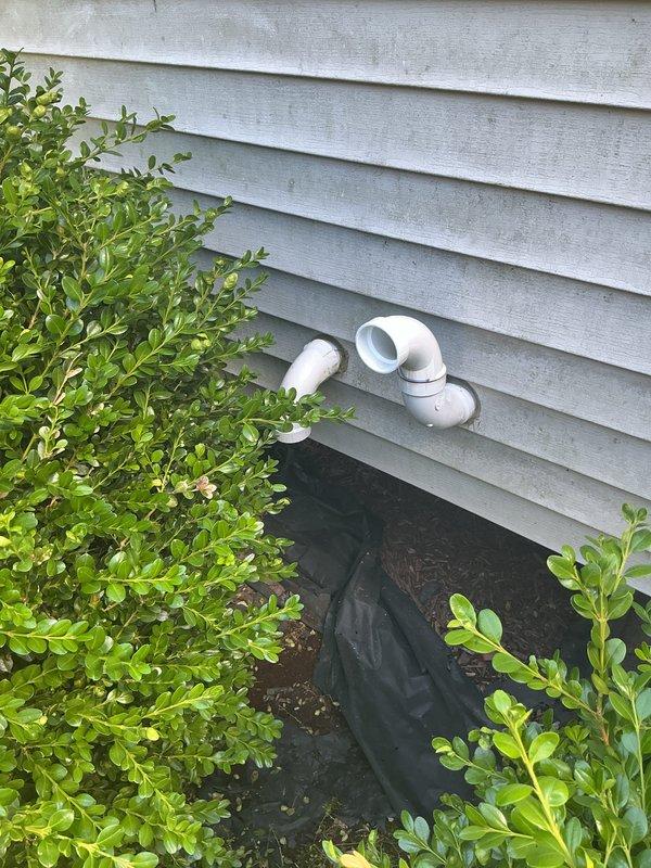 Completed installation of new air conditioning system with evaporator coil. Installed condensate drain assembly with PVC piping and grated trap in interior utility area, routing drainage line through exterior wall with proper pitch for efficient moisture removal. Configured exterior PVC vent penetration through vinyl siding with appropriate weatherproofing and landscape fabric protection at grade level.