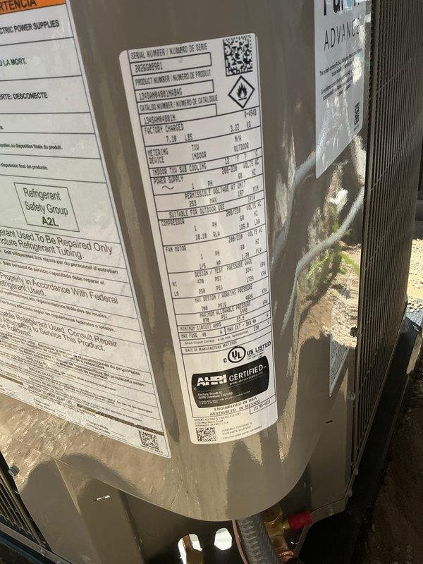 Completed installation of new A2L refrigerant HVAC air conditioning unit at residential property. Unit was transported from shop and installed on exterior pad with proper refrigerant lines, electrical connections, and condensate drainage routed through PVC piping into basement or crawl space area. System tested and verified operational with all safety labels and AHRI certification visible on equipment.