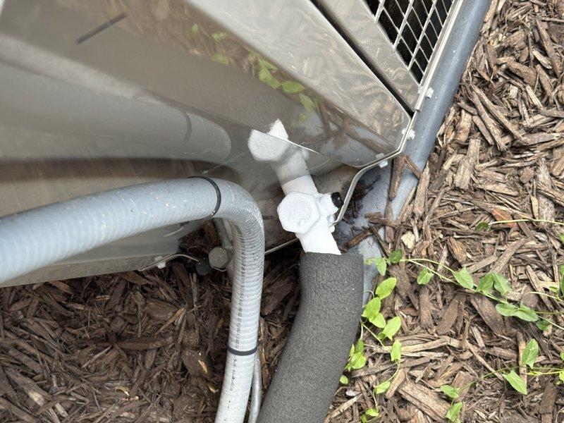 Responded to customer report of water leakage from AC unit. Upon arrival, observed water appearing to originate from condensation drainage system with visible pooling inside the unit cabinet. Opened service access panel and inspected interior components, including evaporator coil assembly and drain pan. Photographed exterior condensate drain line configuration showing PVC piping and corrugated drainage tubing at ground level. Documented interior refrigerant line routing and evaporator coil condition. Initial diagnostic inspection completed to identify source of water accumulation within unit housing.