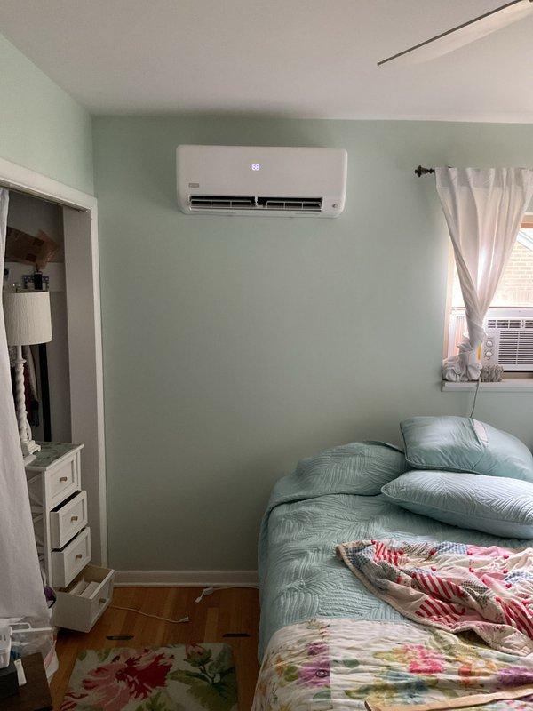 Completed installation of ductless mini-split air conditioning system in residential bedroom. Mounted indoor wall unit above bed area with proper clearance and positioning for optimal airflow distribution, installed outdoor condenser unit on exterior brick wall with secure mounting brackets, and ran refrigerant lines and electrical connections between indoor and outdoor components per manufacturer specifications.