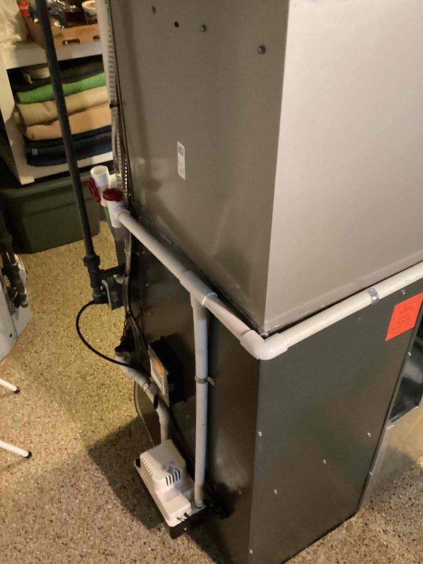 Completed installation of new air conditioning system with evaporator coil in residential basement utility area. Installed gray metal air handler unit in vertical configuration with proper condensate drainage system including white PVC piping and condensate pump with safety switch. Connected all refrigerant lines, electrical components, and drainage systems per manufacturer specifications to ensure optimal system performance and code compliance.