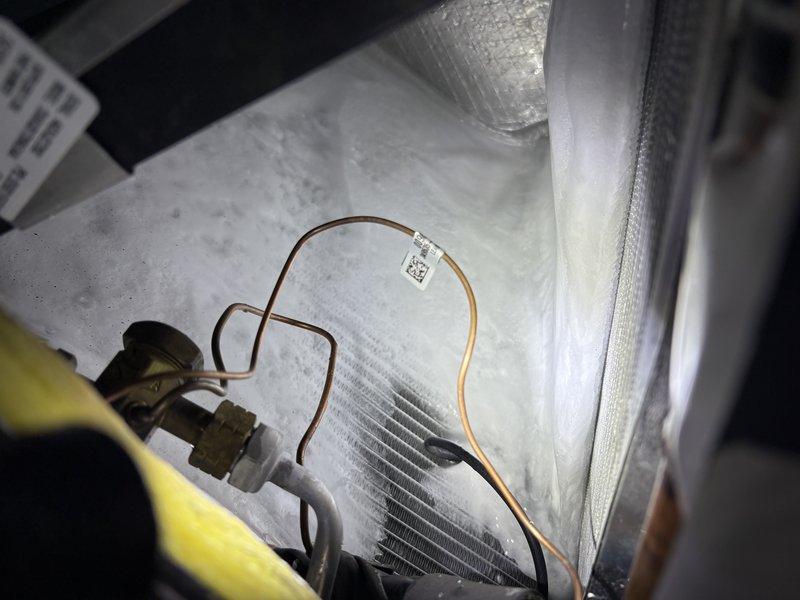 Responded to no cooling complaint on residential AC system under full warranty coverage. Upon arrival, found outdoor condenser unit heavily obstructed by overgrown vegetation restricting proper airflow to coil surfaces. Cleared dense weeds, grasses, and plant growth from around unit perimeter and removed debris from top grille area. Inspected indoor evaporator coil and refrigerant lines, noting moisture accumulation on interior panels consistent with normal operation. Verified refrigerant line connections and insulation integrity. System tested and confirmed operational with adequate airflow restored to condenser. Advised property owner on importance of maintaining minimum 24-inch clearance around outdoor unit for optimal performance and equipment longevity.