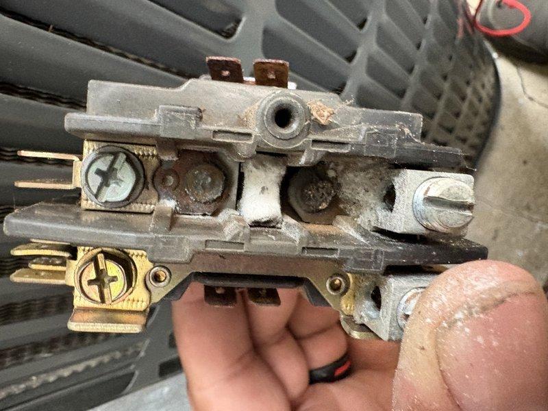 # HVAC Service Call - No Cool Condition

Responded to a no cooling complaint on a commercial HVAC unit. Upon arrival, conducted visual inspection of the outdoor condensing unit and electrical control components. Found evidence of significant weathering and environmental exposure on the equipment exterior and control assembly.

Performed electrical diagnostics on the contactor and relay assembly. Identified a failed contactor with visible signs of deterioration, including corroded brass terminals, oxidized contact points, and accumulated carbon deposits on the contact surfaces. The component showed extensive wear from prolonged service, with tarnished terminals and darkened connection points indicating electrical arcing and poor contact integrity.

Removed the defective contactor from the control panel assembly. Inspected associated wiring connections, including multiple control circuits identified by red, black, orange, yellow, purple, green, and blue conductors. Verified wire terminat