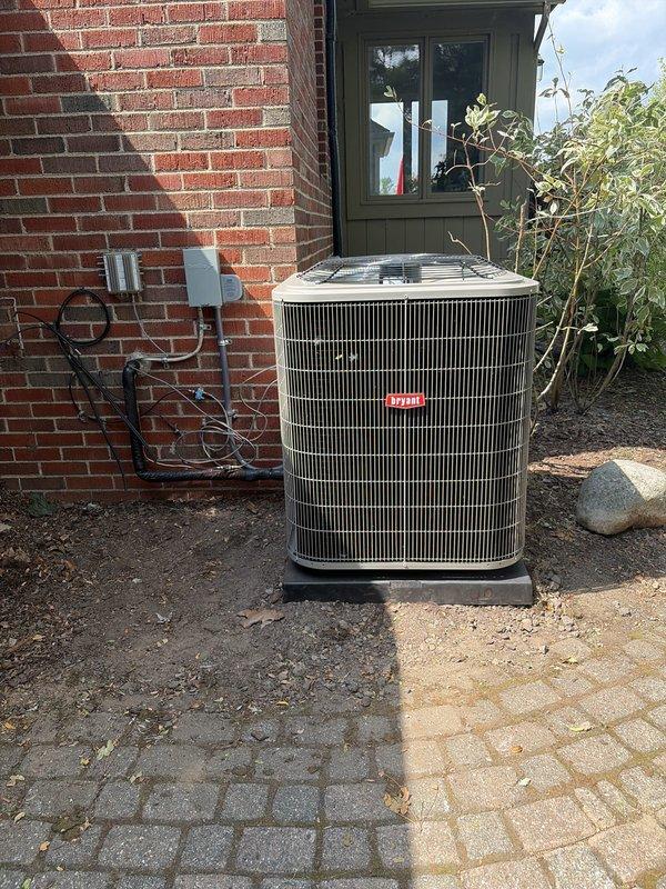Completed installation of new outdoor air conditioning unit and evaporator coil system. The outdoor condenser unit was positioned on a protective plastic pad against the building exterior, with refrigerant lines properly connected through the wall penetration and secured to existing electrical infrastructure. All components were installed to manufacturer specifications, system was tested for proper operation, and the installation site was left clean and ready for service.