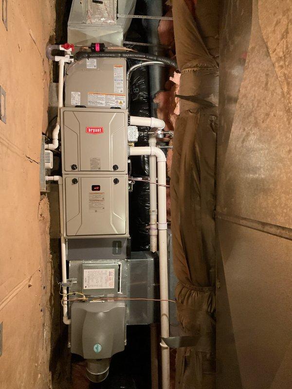 Completed full HVAC system installation including Bryant furnace, air conditioning condenser unit, and humidifier in basement utility area. Installed outdoor condenser on plastic pad against exterior wall with proper refrigerant line set penetration through siding and electrical disconnect box mounted adjacent to unit. Interior installation included furnace with integrated humidifier assembly, PVC venting system, condensate drain lines, and flexible ductwork connections. All equipment installed per manufacturer specifications with proper clearances and secured mounting. System tested and operational upon completion.