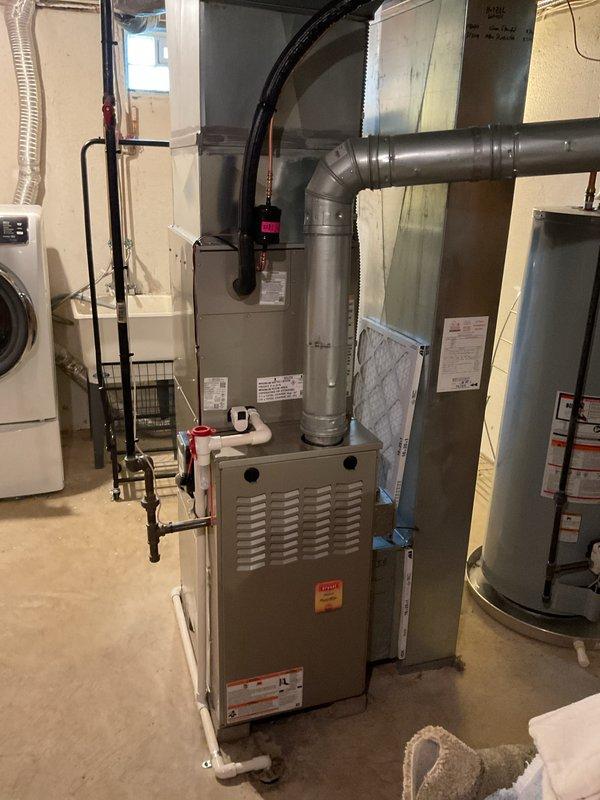 Completed installation of Bryant air conditioning system including outdoor condenser unit and indoor evaporator coil. Outdoor unit was positioned on rubber isolation pad adjacent to home exterior with proper clearances maintained, electrical disconnect and line set connections established per manufacturer specifications. Indoor evaporator coil was integrated with existing furnace system in basement mechanical room, with refrigerant lines and condensate drainage properly installed. All electrical connections, refrigerant charging, and system startup procedures were completed and verified for proper operation.