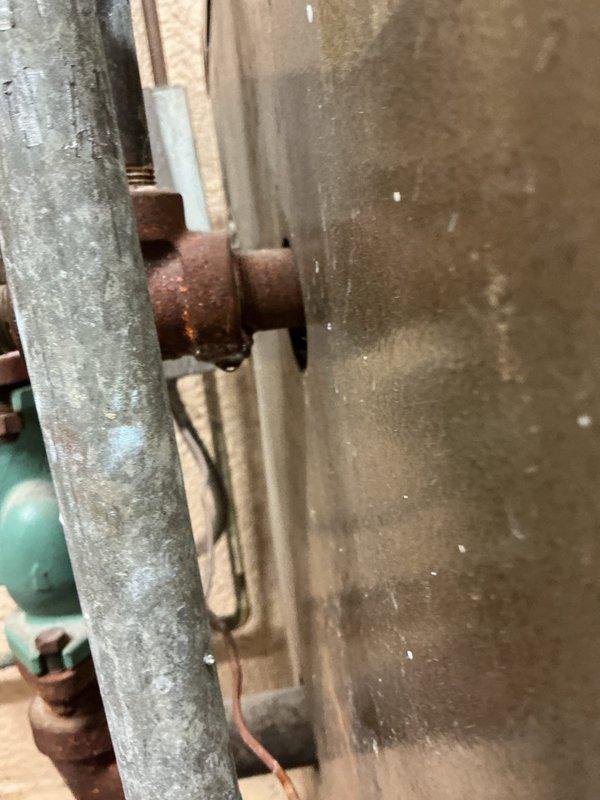 Responded to service call for water leak at boiler system. Upon inspection, identified heavily corroded bolt and fitting assembly on pipe connection near boiler unit with extensive rust damage from prolonged moisture exposure. Leak was actively dripping into collection bucket placed beneath affected area. Assessed deteriorated galvanized piping and compromised connection integrity due to oxidation. Documented existing conditions including rusted components and aging plumbing infrastructure for repair recommendations.