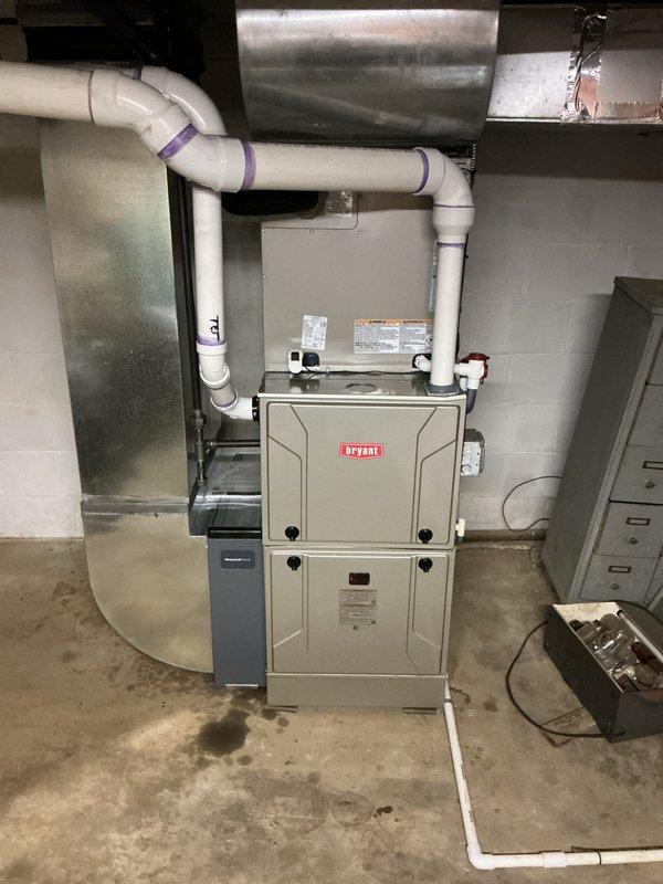 Completed full HVAC system installation including Bryant furnace in basement utility space and matching Bryant condenser unit on exterior concrete pad. Furnace installation included proper PVC venting configuration with multiple elbows for exhaust and intake, metallic supply ductwork connection, humidifier integration, and electrical panel wiring. Exterior condenser positioned on mounting pad against brick wall with gray PVC refrigerant line set properly secured to building with mounting brackets and electrical disconnect box installed per code requirements. All equipment tested and operational upon completion.