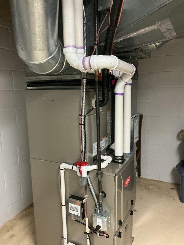 # HVAC Install - Complete System

Completed full HVAC system installation in basement utility area. Installed new furnace/air handler unit mounted against concrete block wall with proper clearances and structural support. Ran and secured copper refrigerant lines from outdoor condensing unit to indoor air handler. Installed metallic flex conduit for electrical connections between equipment and power source.

Configured complete condensate drainage system including white PVC drain lines with proper pitch and purple primer at all joints. Mounted condensate pump on floor with drain pan to collect and discharge water produced by system operation. Installed red-handled shutoff valve on drain line for maintenance access. Secured all drain piping to wall structure with appropriate hangers and supports.

Installed electronic control components including thermostat interface module with indicator light and wiring junction box on furnace cabinet. Connected all low-voltage control wiring between c