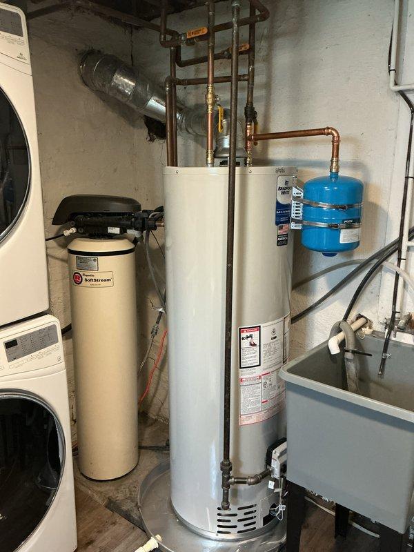 Completed installation of a new tanked water heater in basement utility area. Removed existing unit and installed replacement water heater with proper connections to existing copper supply lines and drainage system. Installed blue expansion tank on wall and connected to plumbing network to accommodate thermal expansion and protect system integrity. Verified all connections for proper operation, tested temperature and pressure relief valve functionality, and ensured compliance with manufacturer specifications and local plumbing codes. System tested and confirmed operational with no leaks detected.