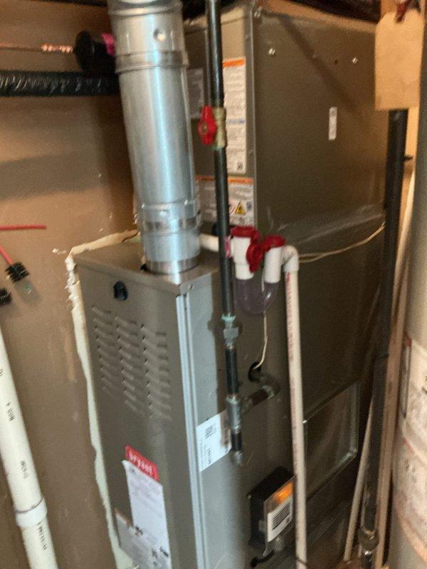 Completed installation of new air conditioning system with evaporator coil in residential utility space. System includes new air handler unit integrated with existing furnace, with all refrigerant lines, condensate drainage via PVC piping to floor drain, and electrical connections properly configured. All equipment tested and operational, with manufacturer labels and safety documentation visible and intact per code requirements.