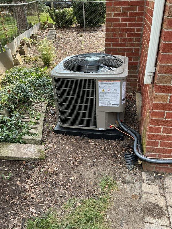 Completed full HVAC system installation including new furnace in basement mechanical room and outdoor condensing unit. Installed gray metal furnace with proper venting using white PVC piping, integrated condensate pump with clear reservoir for drainage management, and connected all necessary ductwork including flexible ducting. Mounted outdoor beige condenser unit on black platform pad against brick exterior wall, ran electrical conduit from unit to building, and installed refrigerant lines between indoor and outdoor components. All equipment properly labeled, secured, and tested for operational functionality upon completion.