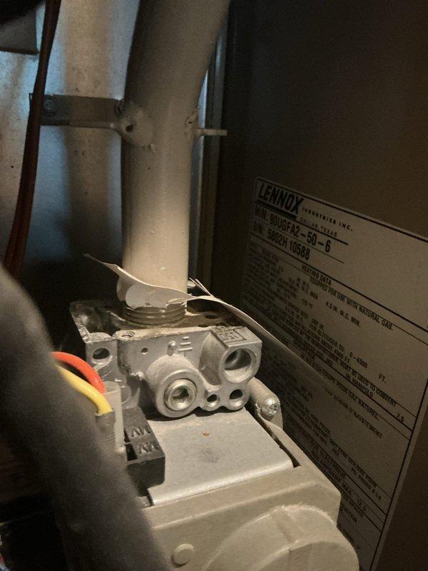 Documented existing HVAC installation featuring a Lennox Model 70E60-6 furnace unit with associated components. Photographed the complete system setup including the beige Lennox furnace positioned beneath a window, gray cylindrical expansion tank with connected piping, gas valve assembly with multiple connection ports, and ductwork configuration. Captured manufacturer specification labels and model identification plates for equipment record purposes.