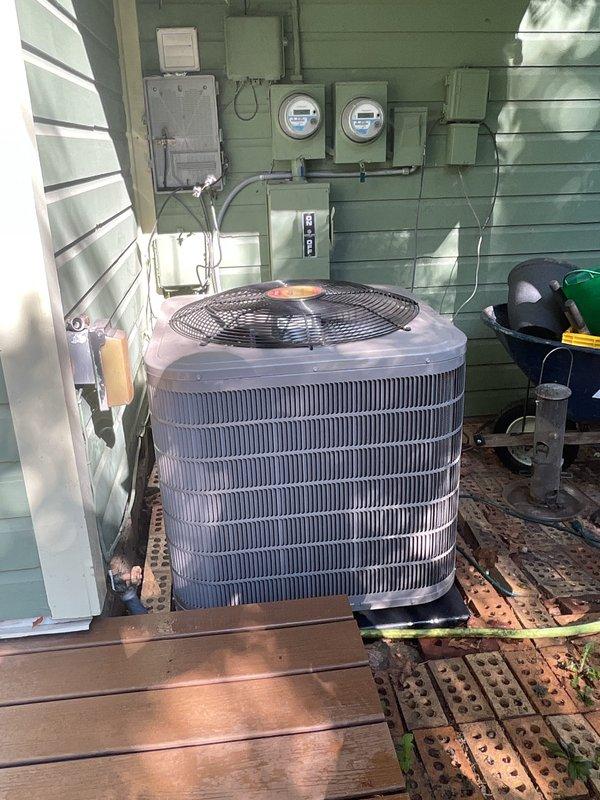Completed scheduled maintenance tune-up on residential air conditioning system and tankless water heater. Performed comprehensive inspection of outdoor cylindrical condenser unit, verified proper operation of heat exchanger coils and fan assembly, and documented equipment condition with photographs showing unit mounted on wooden platform against exterior wall with associated electrical components including meters and disconnect panel.
