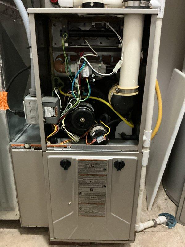 Completed follow-up tune-up service on residential HVAC system. Cleaned outdoor condenser coils using extended 100-foot hose to remove accumulated dirt and debris from vertical grille fins. Inspected indoor furnace components with access panel removed, verifying proper operation of blower motor, electrical connections, gas line, and PVC condensate drainage system—all components found in normal working condition.