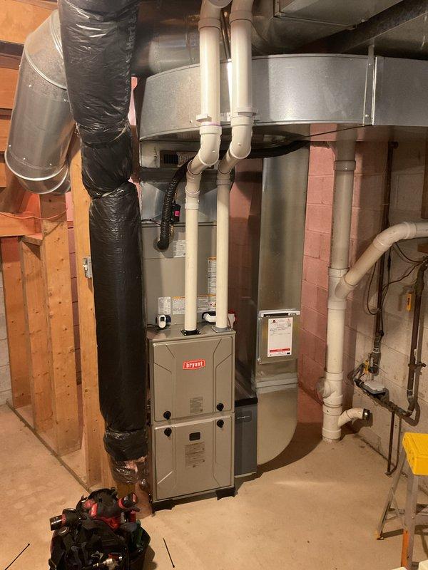 Completed full HVAC system installation in basement mechanical room, including new Bryant forced-air furnace and Carrier air conditioning unit (Model CVAVA4217XMAEB8A). The AC unit utilizes R-454B refrigerant with operating pressure specifications of 870 PSIG/5998 kPa. Installed complete PVC venting system with multiple intake and exhaust pipes routed vertically from furnace unit. Connected black flexible insulated ductwork to sheet metal plenum for proper air distribution throughout the residence. All equipment properly mounted, leveled, and secured in accordance with manufacturer specifications and local building codes. System tested and verified operational upon completion.