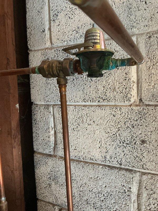 Responded to no cooling complaint on residential air conditioning system. Upon arrival, discovered tenant had been unplugging unit, preventing normal operation. Inspected boiler system and identified active leak at corroded green valve body showing significant oxidation and verdigris buildup on copper piping assembly. Documented condition of plumbing manifold system with multiple branch lines, noting weathered copper pipes with varying patina levels and corroded brass fittings throughout installation. Advised on necessary repairs for leaking valve and proper AC operation procedures.