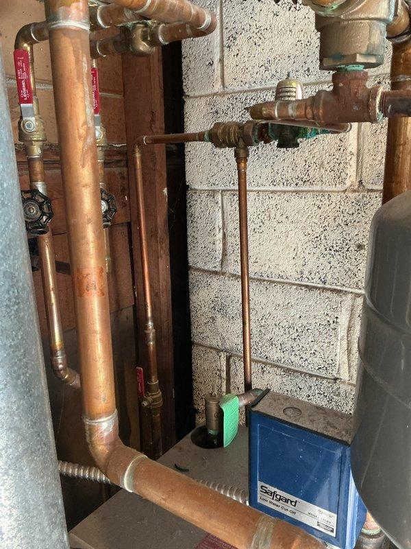 Responded to no cooling complaint on residential air conditioning system. Upon arrival, discovered tenant had been unplugging unit, preventing normal operation. Inspected boiler system and identified active leak at corroded green valve body showing significant oxidation and verdigris buildup on copper piping assembly. Documented condition of plumbing manifold system with multiple branch lines, noting weathered copper pipes with varying patina levels and corroded brass fittings throughout installation. Advised on necessary repairs for leaking valve and proper AC operation procedures.