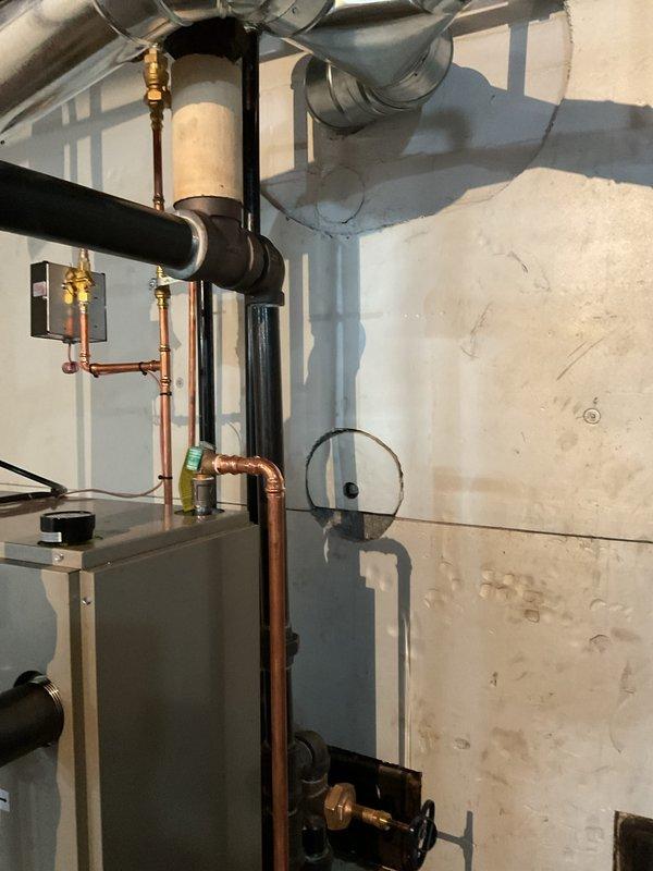 Completed installation of new steam boiler system in residential basement utility area. Installed gray metal boiler unit on concrete pad with proper clearances and connected all required piping including copper supply lines with brass fittings, black insulated steam distribution pipes, and associated pressure relief components. Mounted pressure gauge for system monitoring, ran and secured all ductwork and piping to ceiling joists, and verified proper connections to existing plumbing infrastructure. System tested and operational upon completion.