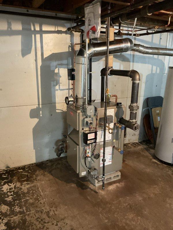 Completed installation of new steam boiler system in residential basement utility area. Installed gray metal boiler unit on concrete pad with proper clearances and connected all required piping including copper supply lines with brass fittings, black insulated steam distribution pipes, and associated pressure relief components. Mounted pressure gauge for system monitoring, ran and secured all ductwork and piping to ceiling joists, and verified proper connections to existing plumbing infrastructure. System tested and operational upon completion.