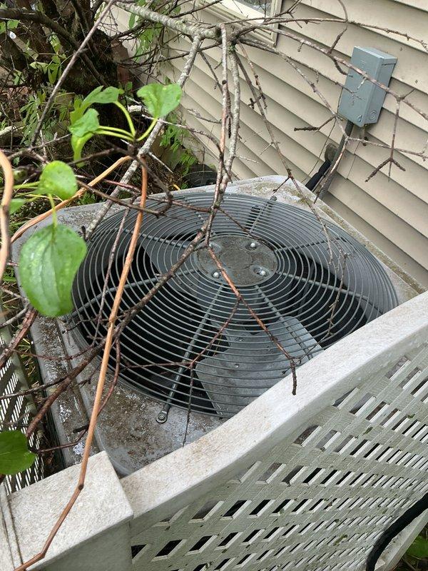Completed scheduled air conditioning tune-up on outdoor condenser unit. Upon arrival, found significant vegetation overgrowth with vines and branches obstructing the fan grille and surrounding the equipment, which could impair airflow and system efficiency. Cleared debris and vegetation from unit to ensure proper operation and ventilation. Performed standard maintenance inspection of condenser components, verified fan operation, and confirmed unit is functioning within normal parameters.