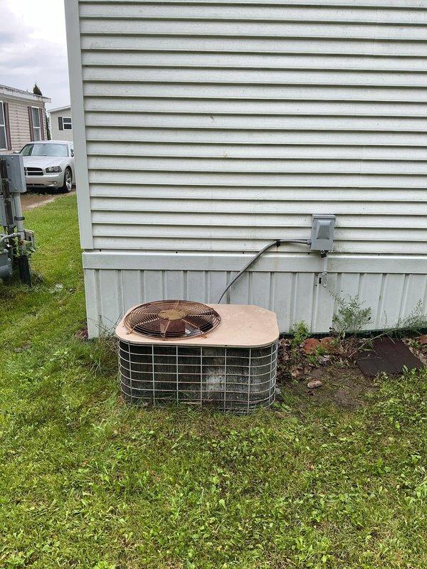 Responded to no cooling complaint at residential property with outdoor condensing unit. Upon arrival, contacted customer via landline as requested before beginning diagnostic assessment. Performed visual inspection of aging AC system exterior components, noting weathered condenser unit with dirt accumulation and discoloration consistent with extended outdoor exposure. Inspected electrical disconnect panel mounted near unit, observing significant rust staining, corrosion, and deterioration from prolonged weather exposure. Documented system condition with photographs showing condenser placement, electrical connections, and overall installation setup. Assessed refrigerant levels and system operation per customer's request to check coolant as potential cause of cooling loss affecting entire home.