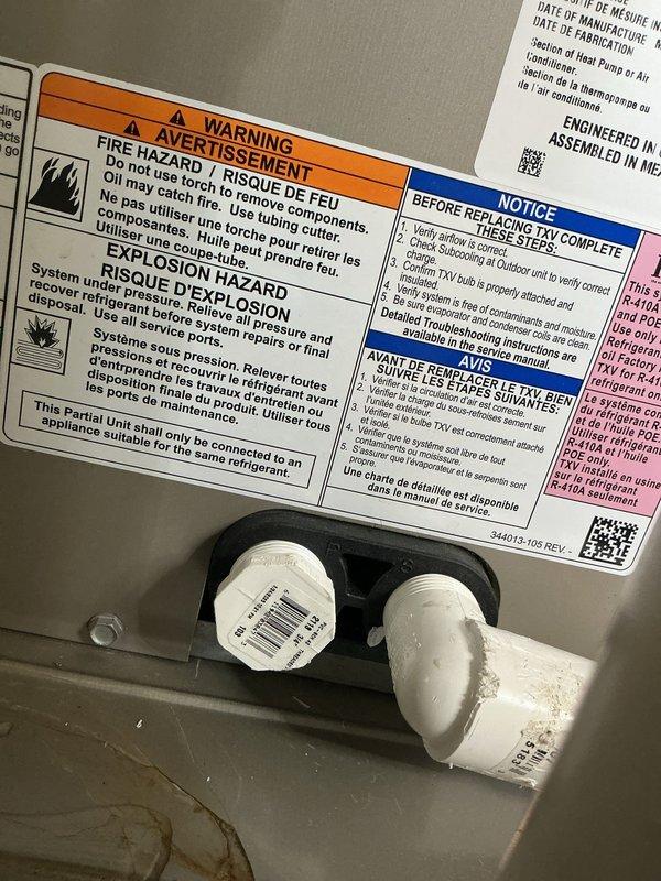 Responded to air conditioning unit leak complaint. Upon inspection, examined refrigerant line connections and drain system components. Documented existing PVC pipe fittings and monitoring equipment mounted to unit housing. Photographed warning labels and refrigerant line connections showing normal wear patterns and minor dust accumulation on system components.