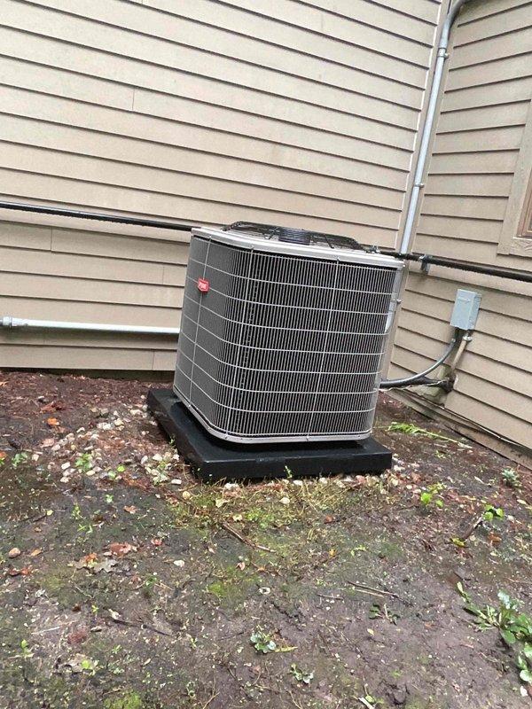 Completed scheduled air conditioning tune-up and preventative maintenance on outdoor condensing unit. Performed comprehensive system inspection, cleaned condenser coils, checked refrigerant lines and electrical connections, verified proper operation of all components, and documented equipment condition with photographs showing unit positioned on pad against building exterior with visible moss growth on surrounding surfaces indicating adequate drainage attention may be beneficial during future visits.