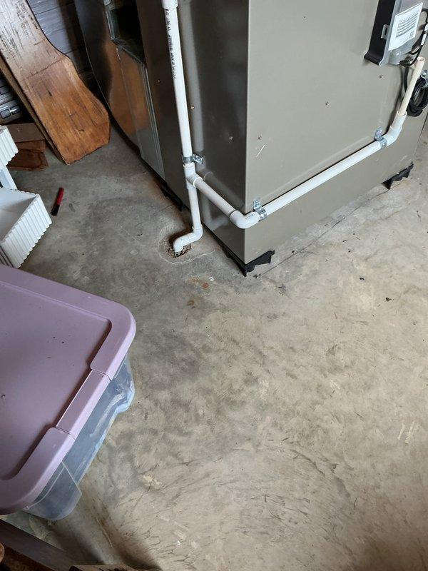 Completed full HVAC system installation including new Bryant outdoor condensing unit and indoor evaporator coil. Installed air handler in utility room with proper drainage lines using white PVC piping with appropriate fittings and connections. Positioned outdoor condenser unit on protective pad against exterior wall with electrical conduit properly routed through siding, verified all connections, and tested system operation for proper cooling performance.