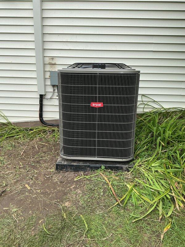 Completed full HVAC system installation including new Bryant outdoor condensing unit and indoor evaporator coil. Installed air handler in utility room with proper drainage lines using white PVC piping with appropriate fittings and connections. Positioned outdoor condenser unit on protective pad against exterior wall with electrical conduit properly routed through siding, verified all connections, and tested system operation for proper cooling performance.