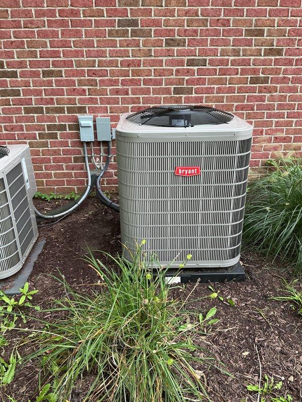 Completed installation of Bryant furnace and air conditioning system. Installed gray Bryant furnace unit in basement utility area with dual white PVC intake and exhaust venting pipes extending vertically from unit. Connected yellow gas line and integrated system with existing ductwork including silver metal ducts and black flexible ducting. Mounted Bryant condenser unit outdoors on concrete pad against brick exterior wall with electrical disconnect box, refrigerant lines, and electrical conduit properly installed and secured. System installation requires follow-up visit to complete re-piping of exhaust venting from flexible to black pipe, install large bypass humidifier, and finalize all connections for full operational status.
