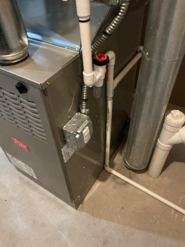 Completed installation of new gas furnace in residential utility space. Installed gray metal furnace unit with proper ventilation and air distribution ductwork, including white PVC piping for condensate drainage and venting system with appropriate valves and fittings. Connected black flexible ductwork to integrate with existing HVAC distribution system. Unit positioned alongside existing water heater to maximize available space while maintaining code-compliant clearances. System tested and verified operational upon completion.