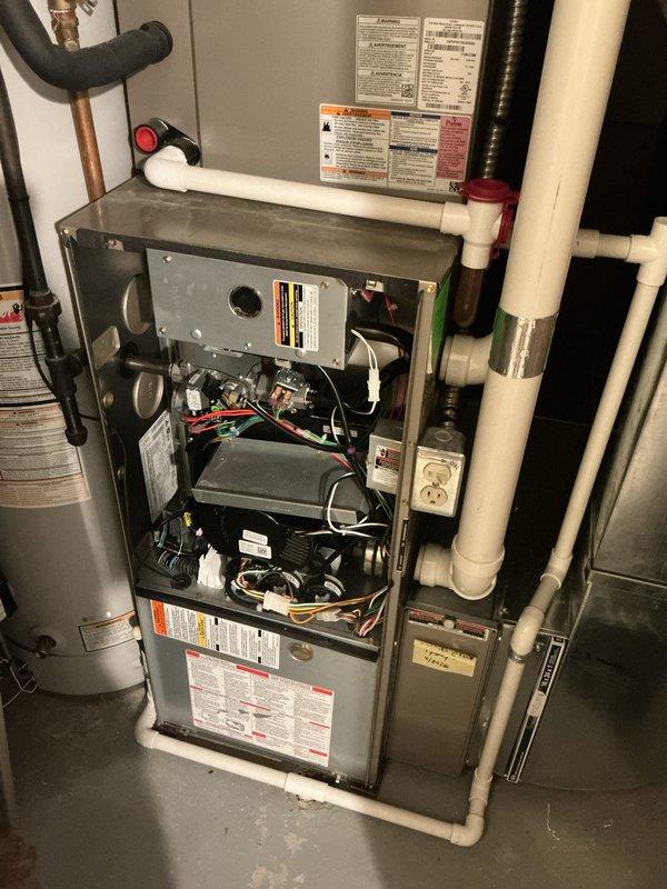 Performed diagnostic assessment of residential HVAC system and scheduled follow-up appointment for thermostat replacement and system tune-up. Documented existing furnace installation with internal components exposed, including blower motor, control boards, wiring, and safety switches. Identified thermostat requiring replacement and possible manufacturer recall requiring verification. Photographed current system configuration showing furnace unit with adjacent water heater, PVC condensate drainage, copper refrigerant lines, and electrical connections for service records. Appointment confirmed for complete thermostat replacement and comprehensive system maintenance tune-up.