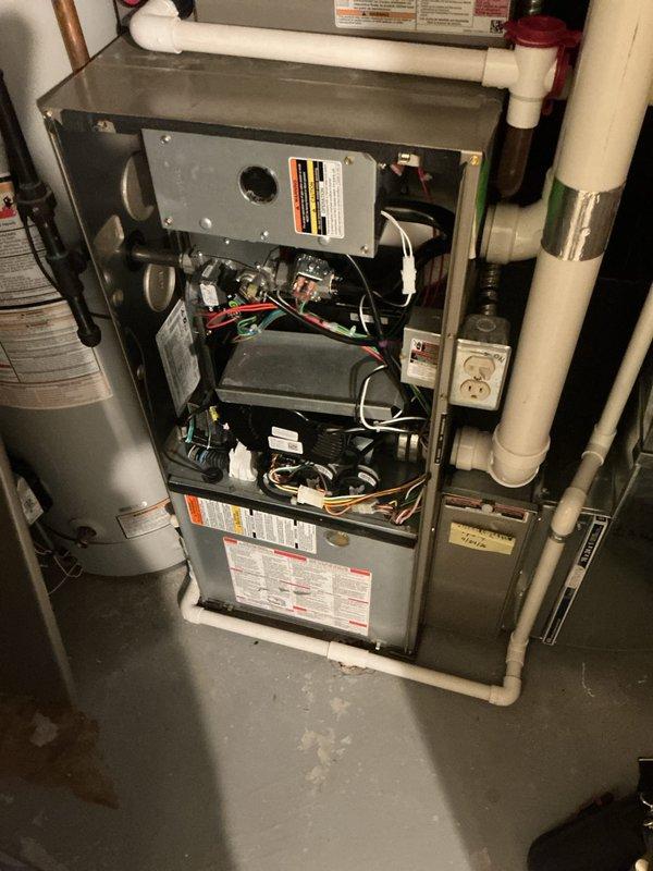 Performed diagnostic assessment of residential HVAC system and scheduled follow-up appointment for thermostat replacement and system tune-up. Documented existing furnace installation with internal components exposed, including blower motor, control boards, wiring, and safety switches. Identified thermostat requiring replacement and possible manufacturer recall requiring verification. Photographed current system configuration showing furnace unit with adjacent water heater, PVC condensate drainage, copper refrigerant lines, and electrical connections for service records. Appointment confirmed for complete thermostat replacement and comprehensive system maintenance tune-up.