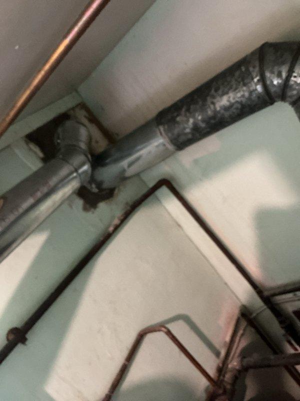 Completed installation of tanked water heater system with new chimney liner in residential utility space. Configured copper supply lines with angular routing to navigate existing mechanical infrastructure, installed proper venting through black flexible duct system, and integrated connections with overhead plumbing network. All components installed to code specifications with secure mounting and proper clearances maintained throughout confined workspace.