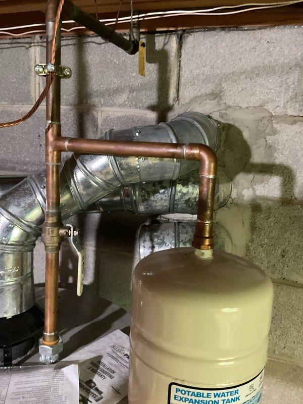 Completed full gas boiler installation in residential basement mechanical room, including all associated plumbing connections, copper piping network with brass fittings and shut-off valves, potable water expansion tank, and proper venting with metal ductwork. Installation includes Defender water heater integration with control systems, galvanized and copper pipe transitions, and complete HVAC infrastructure mounted to concrete block walls with proper support and code-compliant configuration. All equipment tested and operational, with service financing documentation completed and identification verified on file.