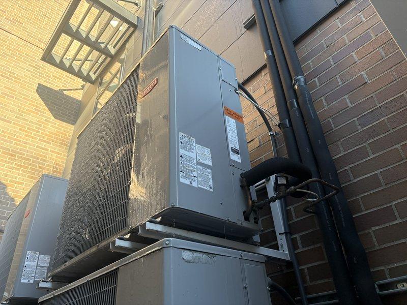 Completed AC tune-up service on exterior-mounted condensing unit and air handler system located on elevated platform against building exterior. Accessed rooftop equipment using extension ladder and performed comprehensive maintenance inspection of multi-unit HVAC installation including refrigerant line checks, electrical connections, and condenser coil assessment.
